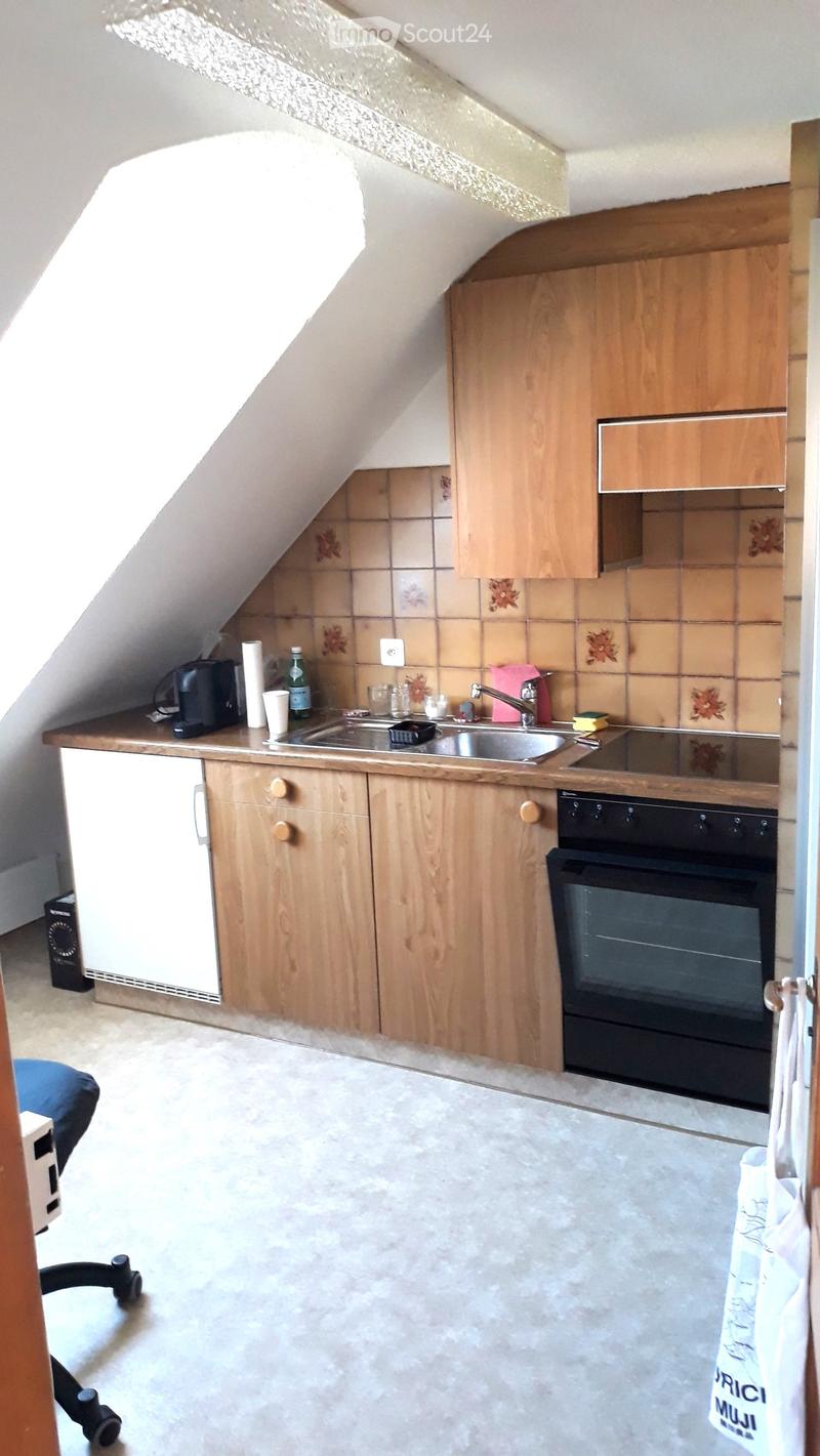Compact kitchen with wooden cabinets, a sink, oven, refrigerator, and various small appliances and items on the counter.