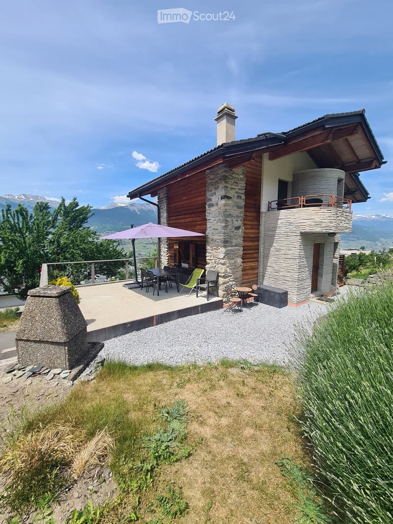Two-story house with stone and wood exterior, balcony, outdoor dining area, and scenic mountain view.