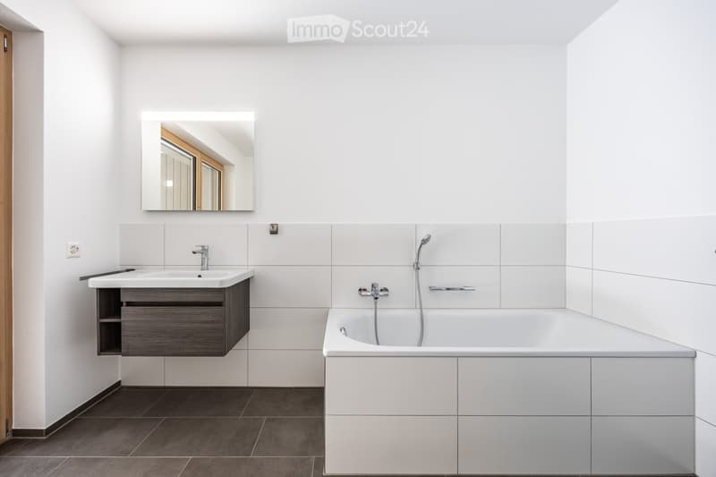 Modern bathroom with white tiles, a dark grey sink cabinet, a large bathtub, and a wall-mounted mirror.