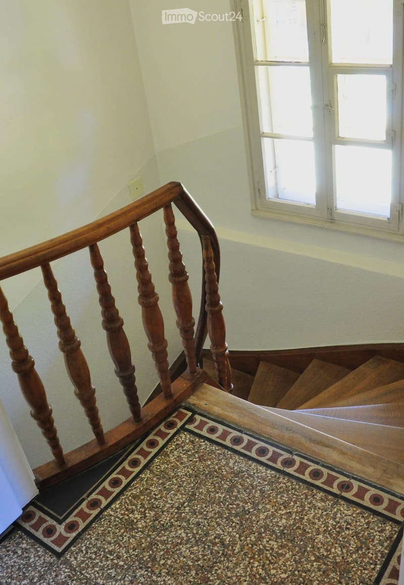 Wooden staircase with a decorative balustrade and patterned tile runner leading upwards, with a window on the right side.