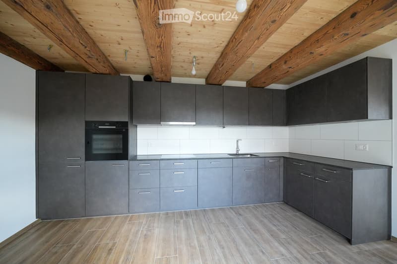Modern kitchen with grey cabinets, wooden ceiling beams, and a stainless steel sink.