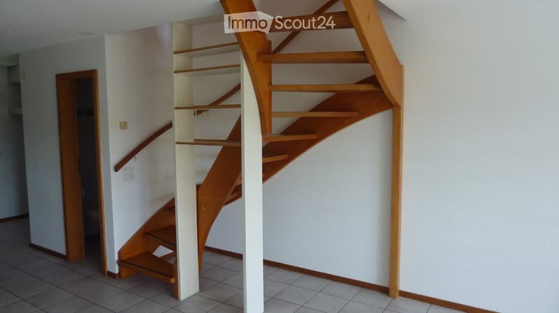 Modern wooden staircase with open design and built-in shelving, leading to an adjacent room.
