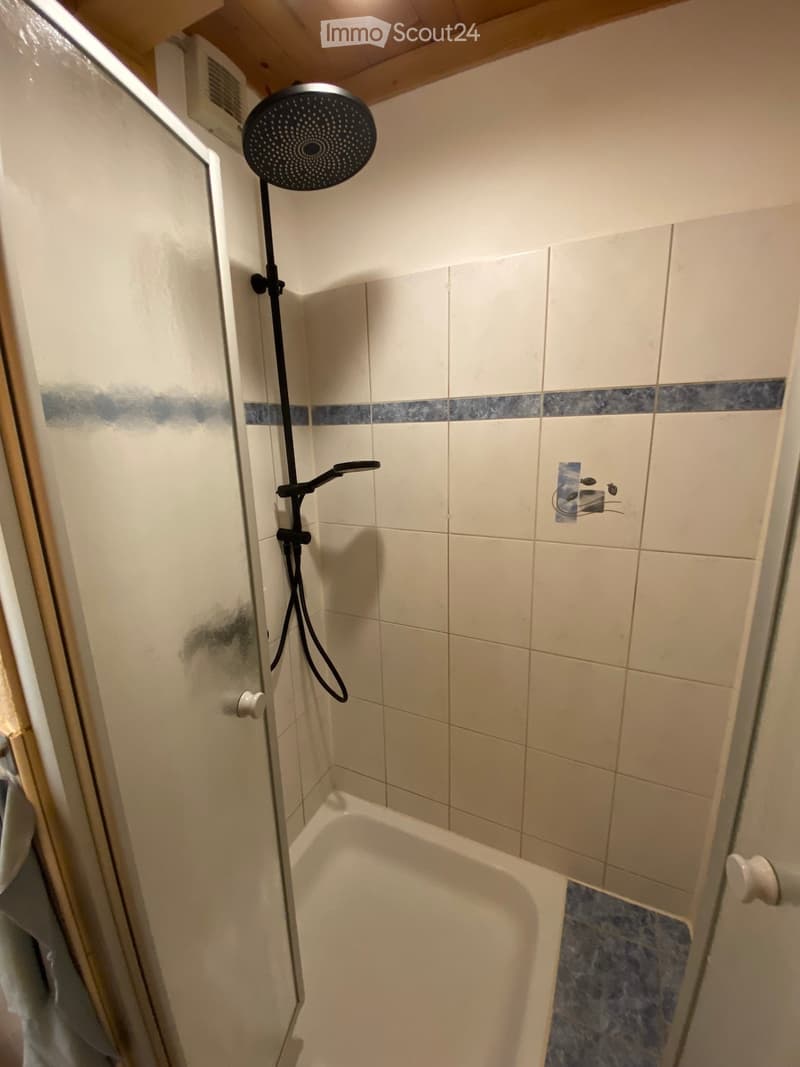 Bathroom with a bathtub, showerhead, and faucet. Tiles are white with a blue accent border.