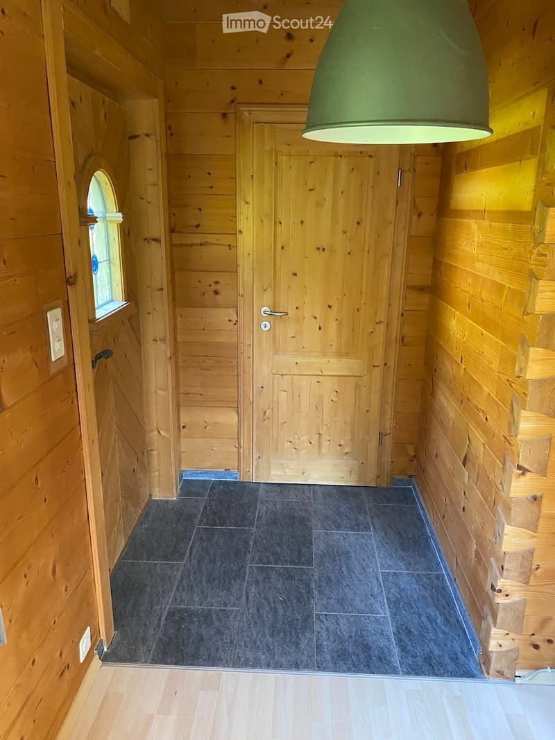 Wooden-walled hallway with dark tiled floor, two doors, and a green pendant light fixture.