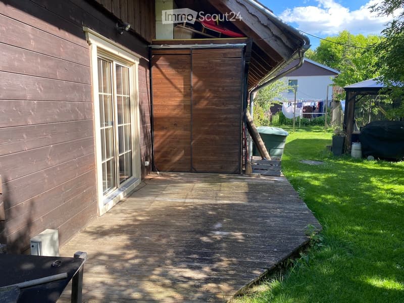 Wooden deck leading to a house with a wooden garage door, grassy yard, clothesline, and outdoor furniture.