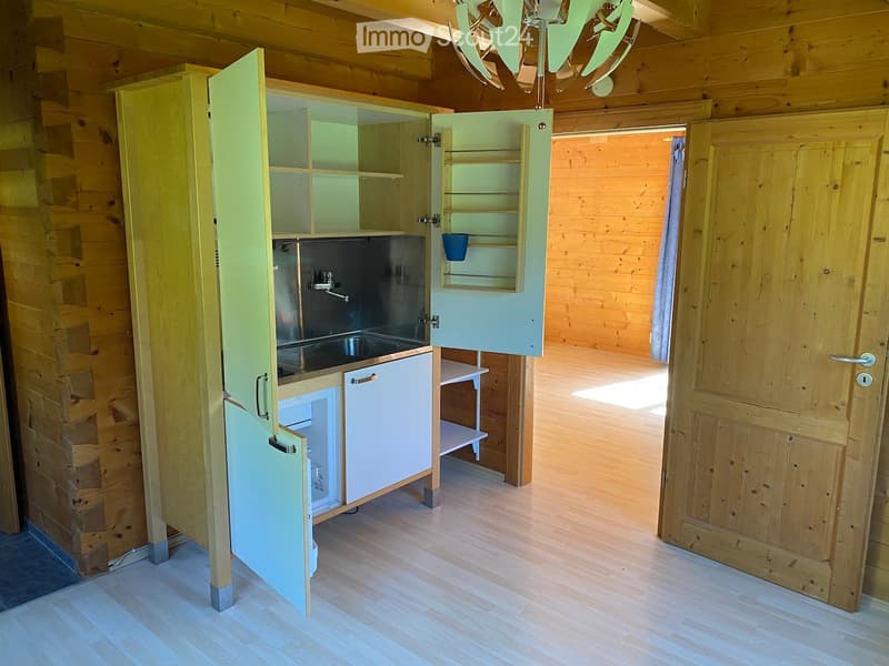 Compact kitchen with wooden walls, a sink, cabinets, and a small refrigerator. A cup is visible on the shelf.