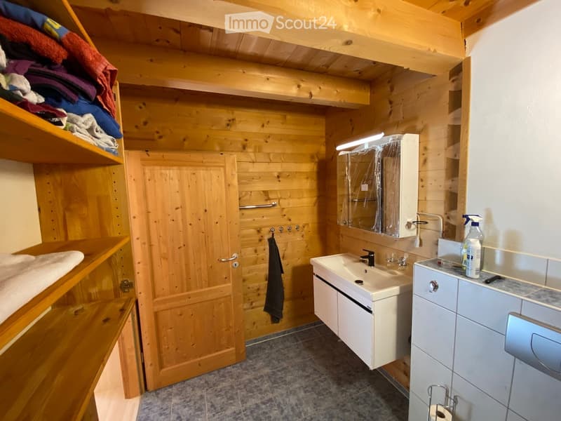 Cozy wooden bathroom with a sink, mirror, cabinet, and shelves holding towels and cleaning supplies.