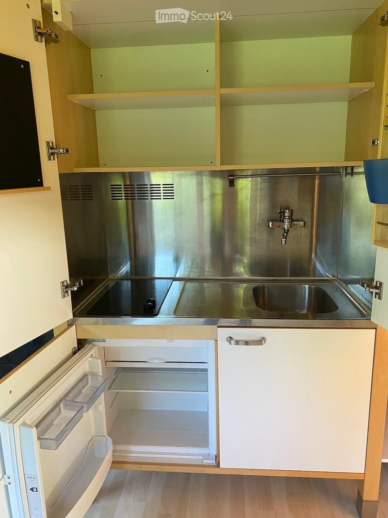 Compact kitchen with stainless steel sink, faucet, and built-in refrigerator. Light wood cabinets and drawers are visible.