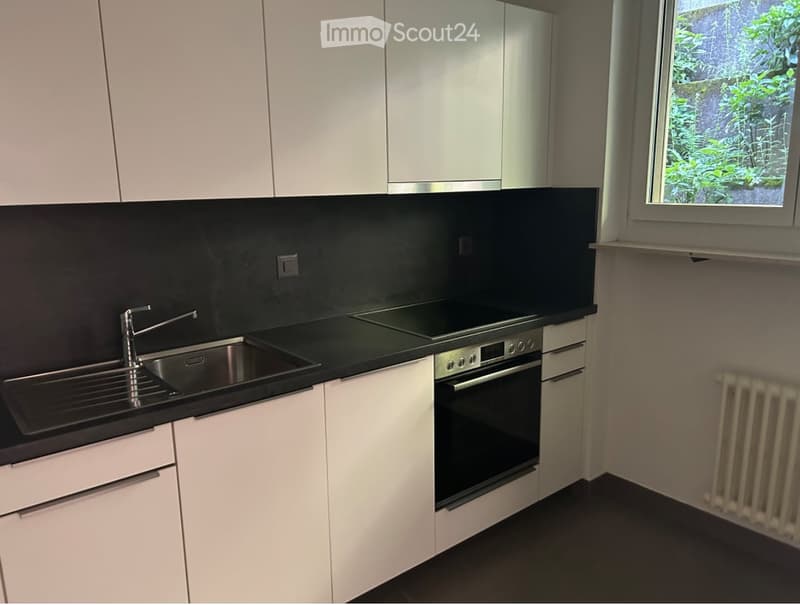 White cabinets, black countertop, sink, faucet, oven, windows, white radiator, kitchen appliances