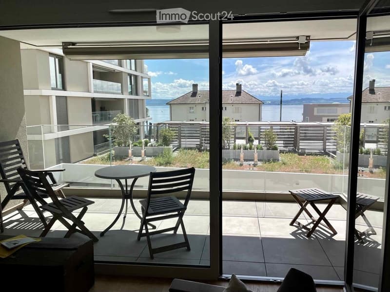 Balcony with a round table and four chairs, overlooking a scenic view of a lake and distant mountains.