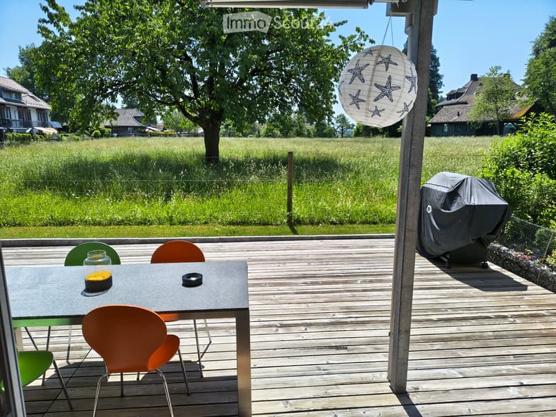Wooden deck with a table and chairs, a covered grill, and a hanging lantern with star designs. The background shows a grassy field and trees.