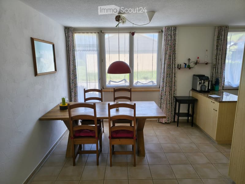 Dining room with a wooden dining table, six chairs, a mirror on the wall, a coffee maker on the counter, and a hanging lamp.