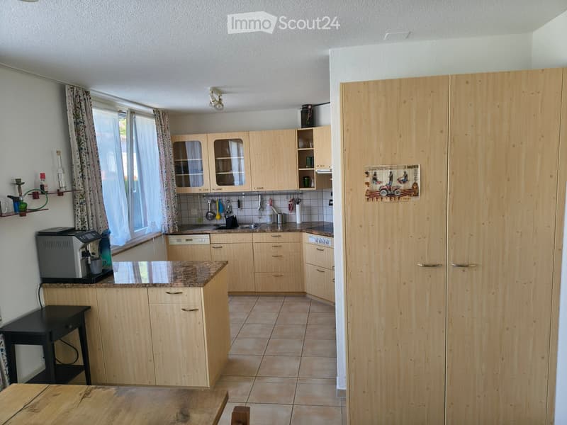 Bright kitchen with light wooden cabinets, granite countertop, and tiled floor. Features a coffee maker, sink, and various kitchen utensils.