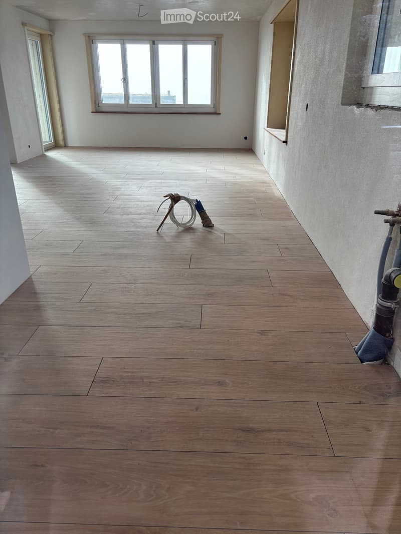 Empty room with wooden flooring, white walls, and large windows allowing natural light. No furniture or equipment present.