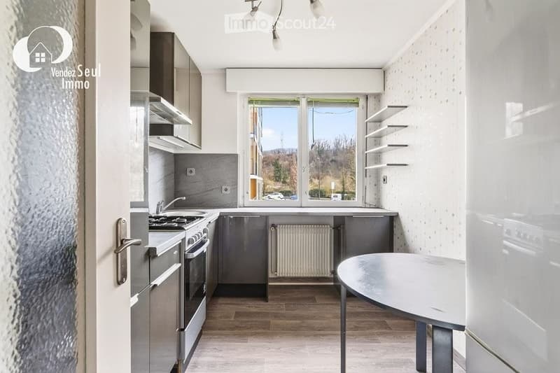 Modern kitchen with stainless steel appliances, wooden flooring, and large windows offering a view of the outdoors.