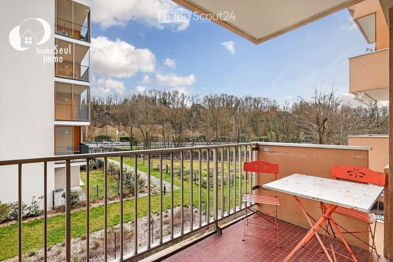 Balcony with a view of a park, featuring a small table and two chairs.