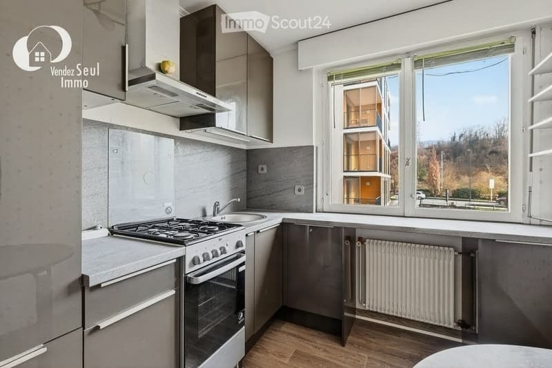 Modern kitchen with stainless steel appliances, including a stove, oven, and sink, fitted cabinets, and large windows offering a view of the building exterior.