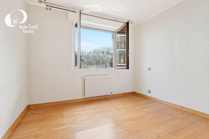 Empty room with wooden flooring, white walls, a radiator, and large windows with blinds. No furniture or equipment present.