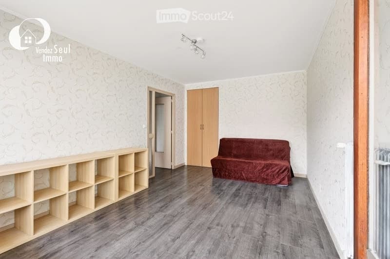 Living room with wooden floor, patterned wallpaper, a red sofa, and a wooden shelf unit.