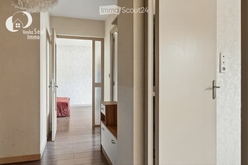 A modern hallway with wooden flooring, white walls, and several doors leading to different rooms. A small wooden cabinet is visible on the right side.