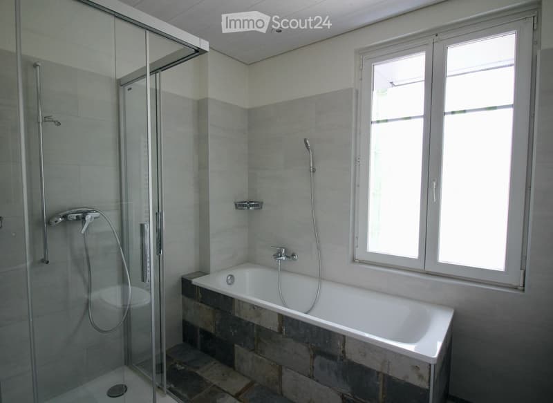 Modern bathroom with a white bathtub, glass-enclosed shower, and large windows providing natural light.