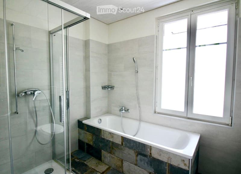 Modern bathroom with a bathtub, glass-enclosed shower, and large window providing natural light.
