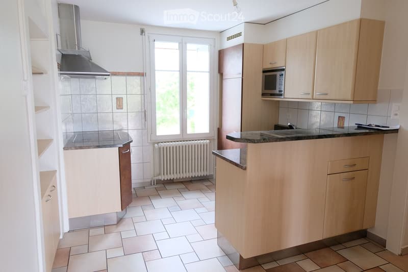 Modern kitchen with light wooden cabinets, granite countertop, microwave, sink, and stove. White tiled floor and walls, with a window providing natural light.