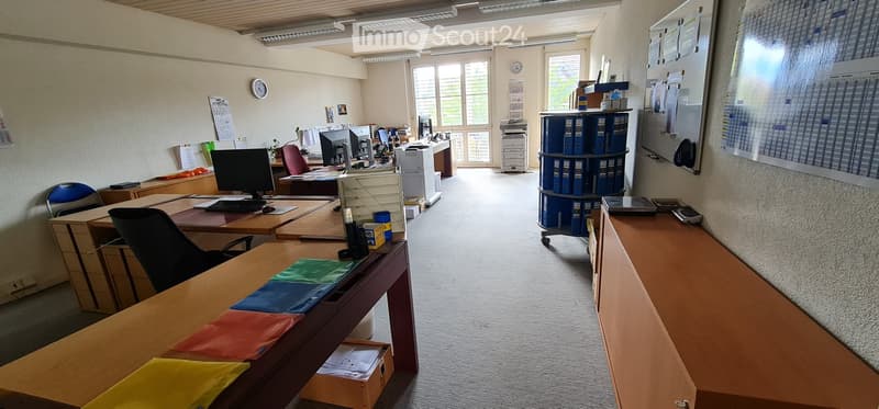 Office space with desks, chairs, computers, a printer, filing cabinet, calendar, whiteboard, and screen.