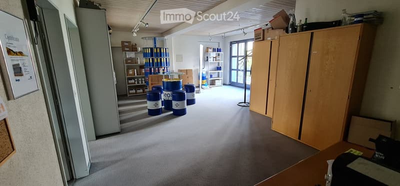 Office or storage area with carpeted floor, large wooden cabinet, shelves with boxes, barrels, and a poster on the wall.