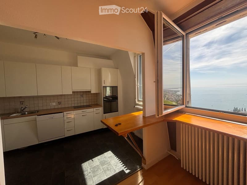 Modern kitchen with white cabinets, stainless steel appliances, and a large window offering a scenic ocean view.