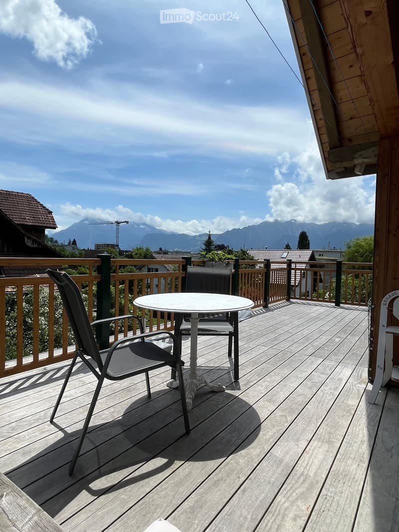 Wooden deck with a round table and chairs, overlooking a scenic mountain view.