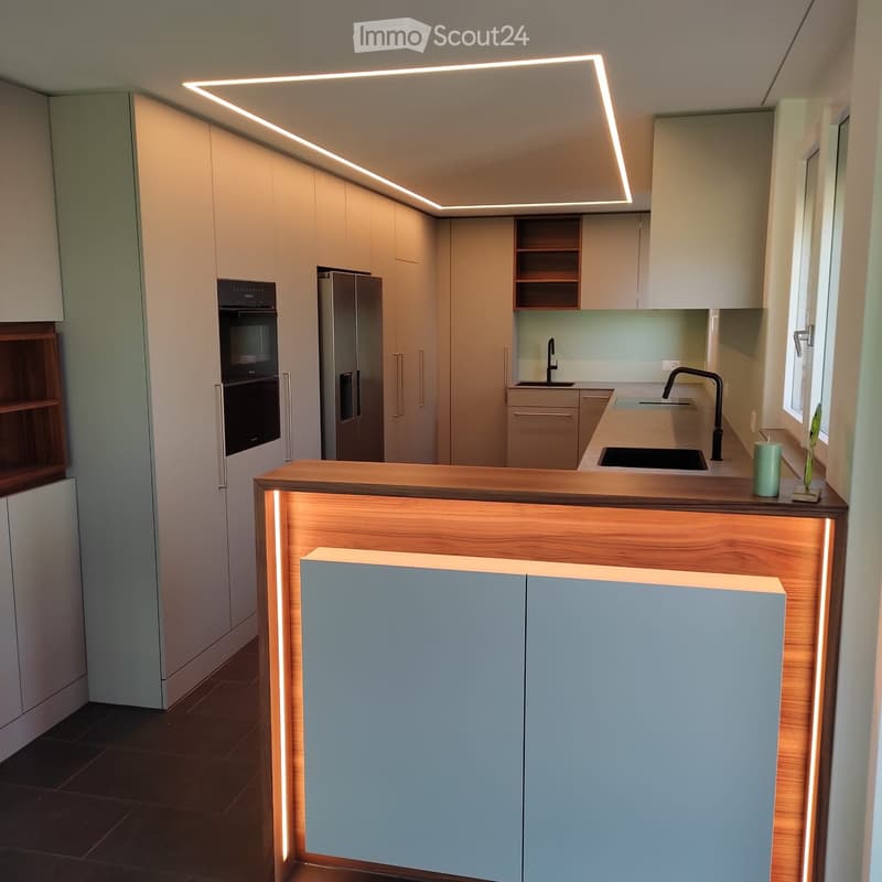 Modern kitchen with light-colored cabinets, stainless steel appliances, and a wooden countertop with integrated lighting. Features a sink with a modern faucet and a small decorative vase on the counter.