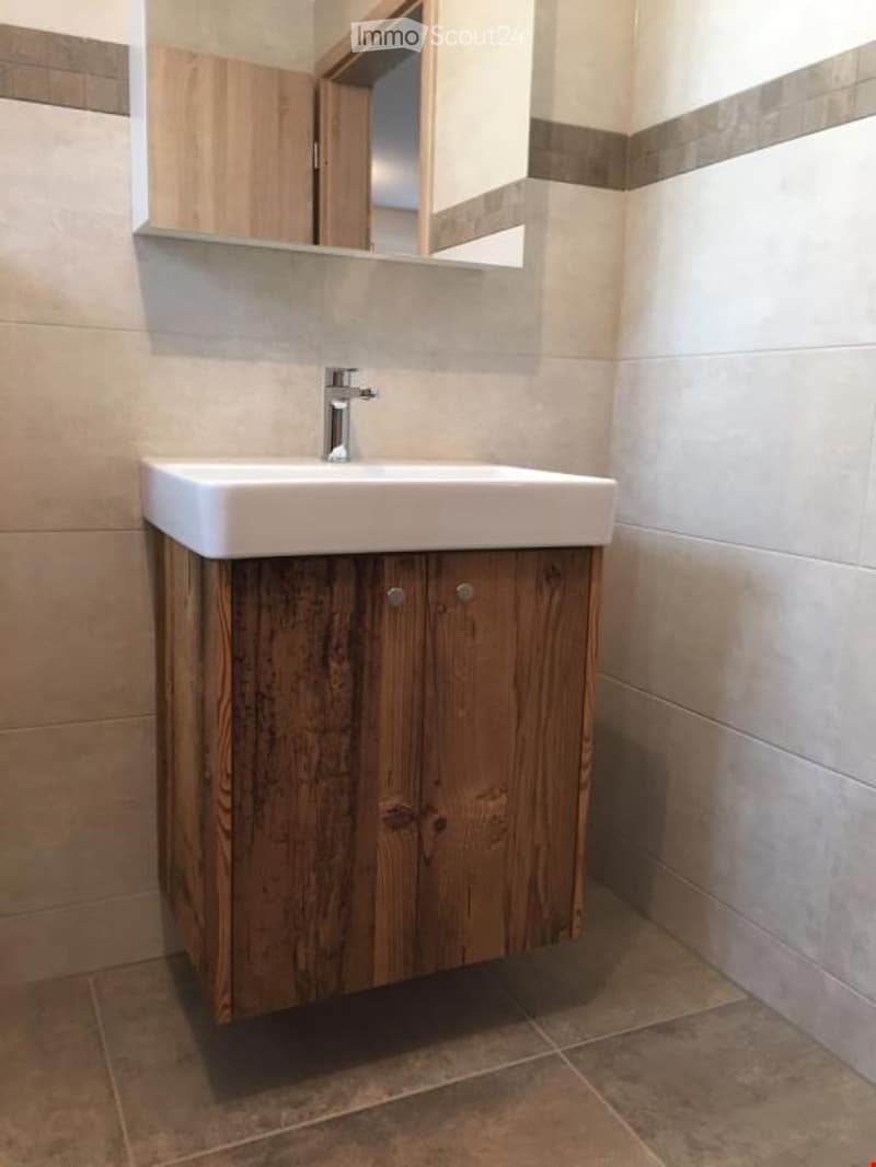 Modern bathroom with a white sink on a wooden cabinet, a mirror above, and tiled walls and floor.