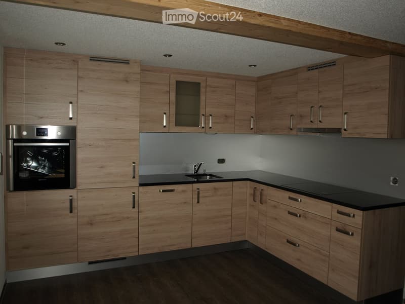 Modern kitchen with light wood cabinets, stainless steel oven, black countertop, and sink.
