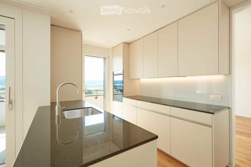 Modern kitchen with white cabinets, dark countertop, stainless steel sink, and a view through a large window.