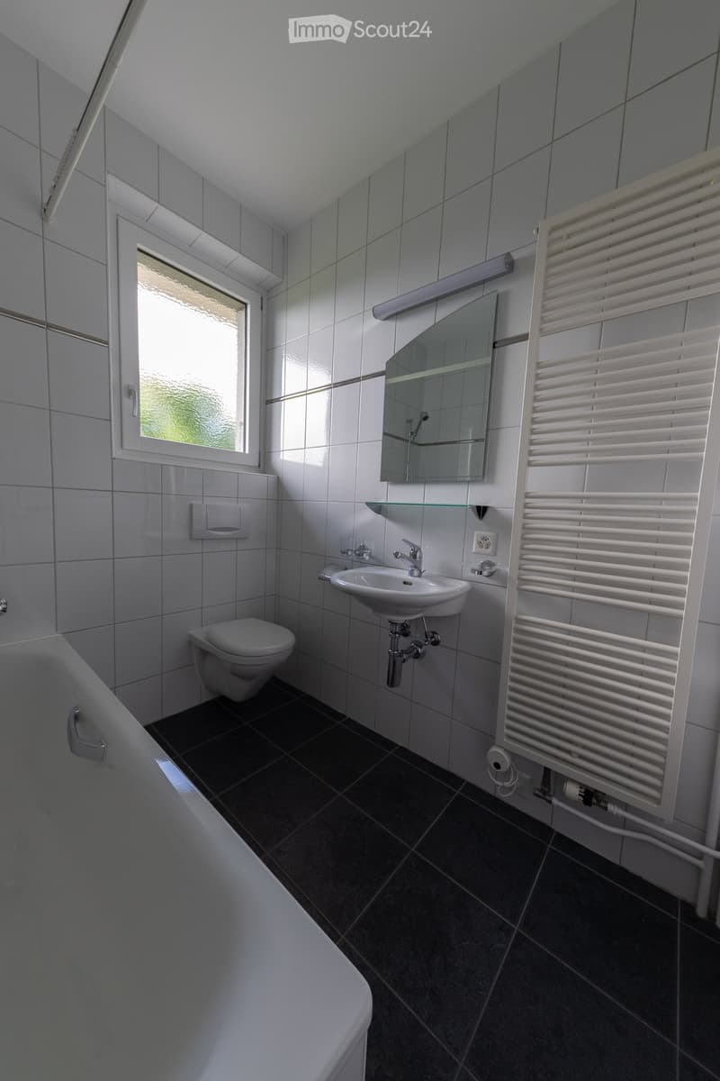Bathroom with white tiles, bathtub, toilet, sink, mirror, and towel rack