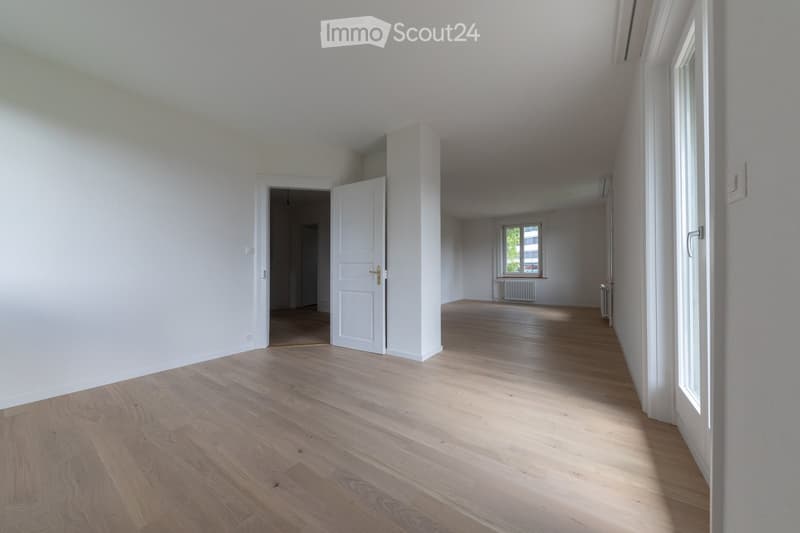 Empty room with white walls, wooden floor, two doors, and windows