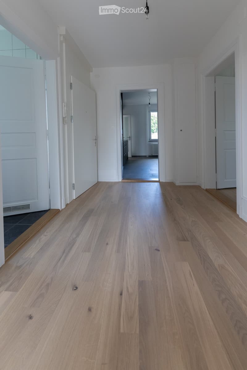 Empty room with hardwood floors, white walls, and open doors leading to other rooms
