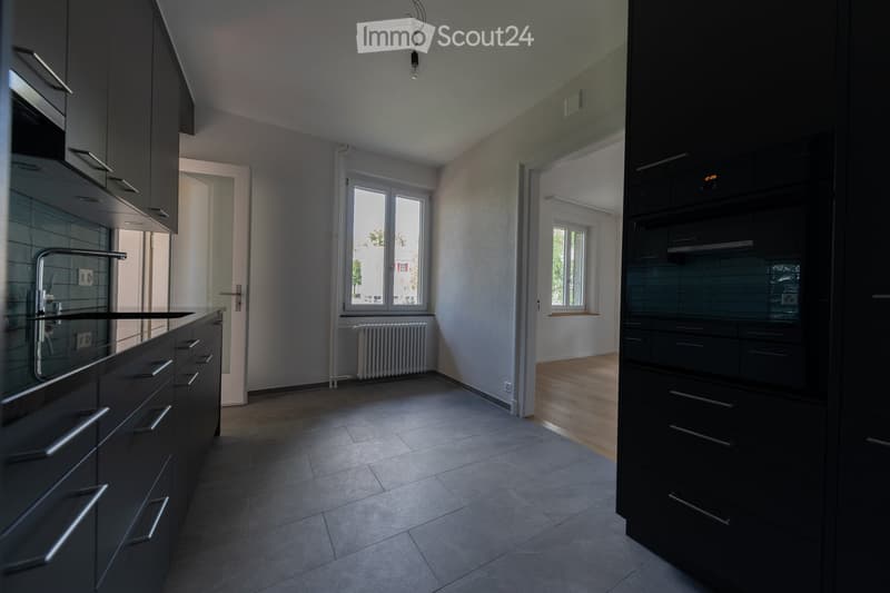 modern kitchen with black cabinets, gray tiled floor, stainless steel sink, white radiator, double windows