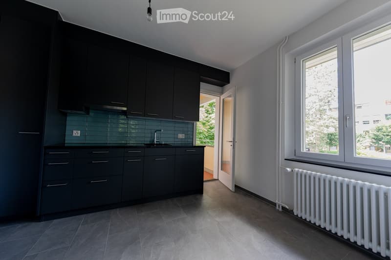 modern kitchen with black cabinets, white tiled floor, sink, faucet, window, radiator