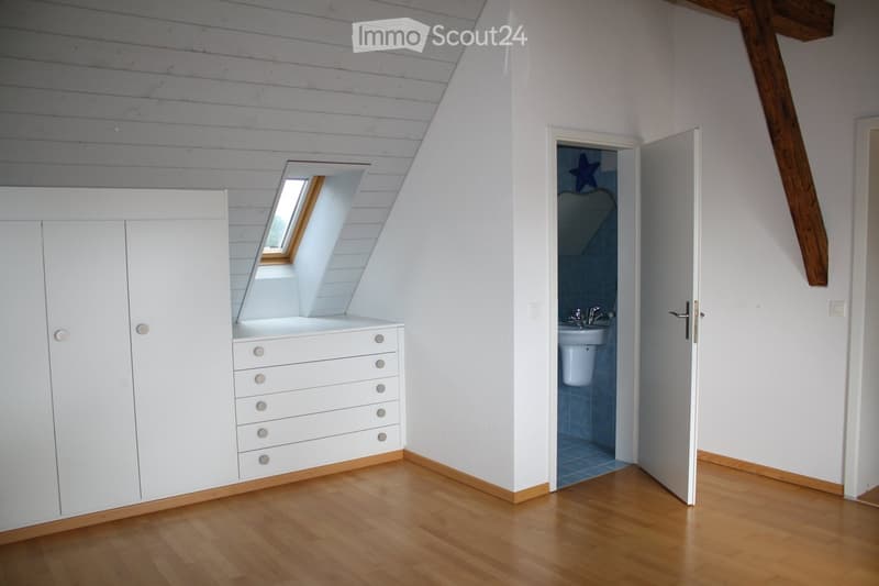 Bright bedroom with wooden flooring, white built-in wardrobe, and an open doorway leading to a small bathroom with a sink and toilet.