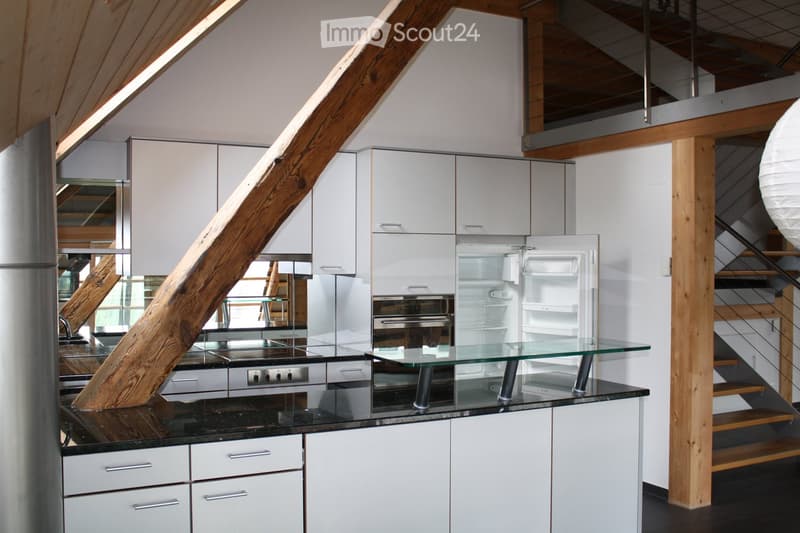 Modern kitchen with white cabinets, stainless steel appliances, a glass island table, and a large wooden beam as a structural element.