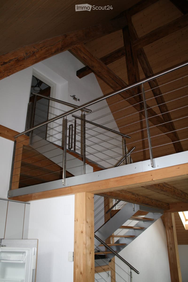 Modern interior with wooden beams, metal railing, and staircase leading to an upper level.