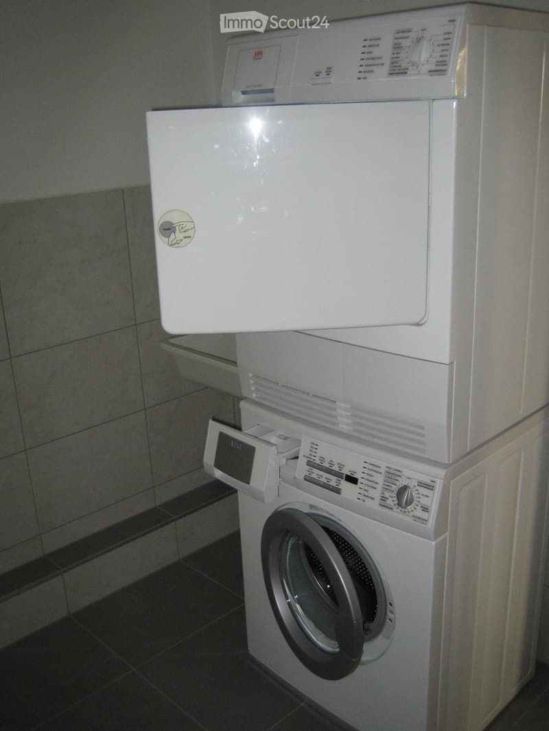 A white washing machine and dryer stacked vertically in a tiled bathroom.
