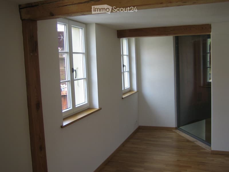 Empty hallway with wooden flooring, white walls, and two windows with wooden sills. The space is clean and unfurnished.