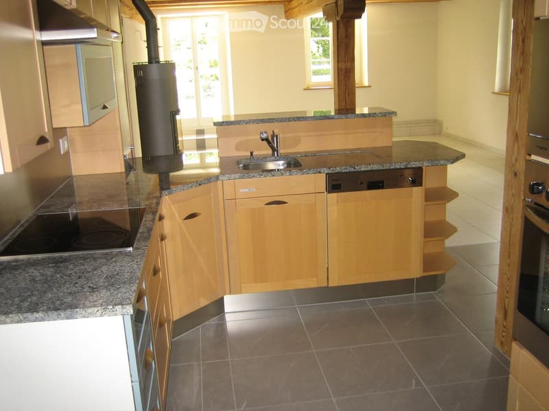 Modern kitchen with light wooden cabinets, granite countertops, stainless steel appliances, and a central island with a sink and dishwasher.