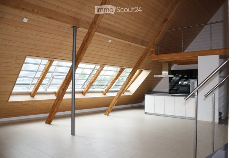 Open-plan attic space with wooden beams, skylights, white kitchen cabinets, and a modern staircase.