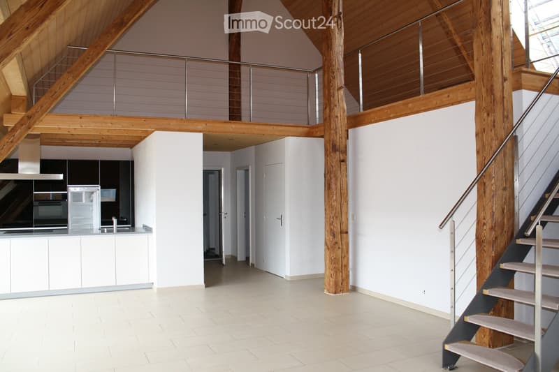 Open-plan living and kitchen area with white cabinets, stainless steel appliances, and a wooden staircase leading to an upper level.