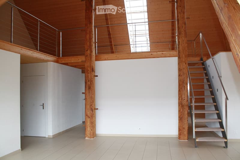 Bright, open hallway with wooden beams, a staircase leading to an upper level, and large windows allowing natural light to fill the space.