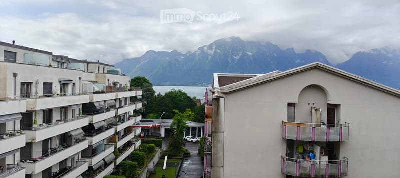 Multi-story residential building with balconies overlooking a scenic lake and mountain backdrop.